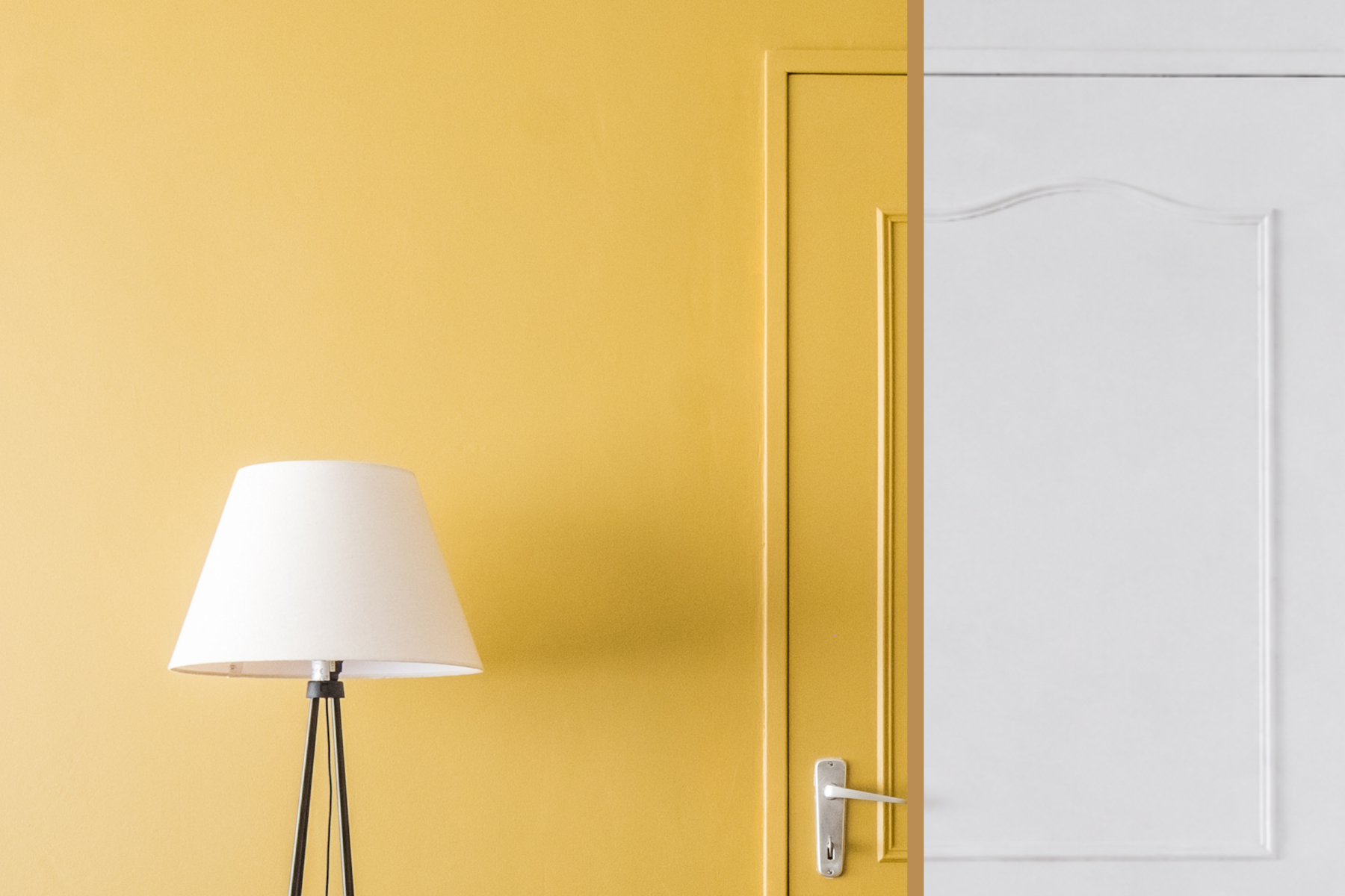 Een witte lampenkap op een zwart driepootonderstel staat naast een gele deur met sierlijke versieringen en gaat naadloos over in een bijpassende gele muur in een minimalistisch, modern interieur.