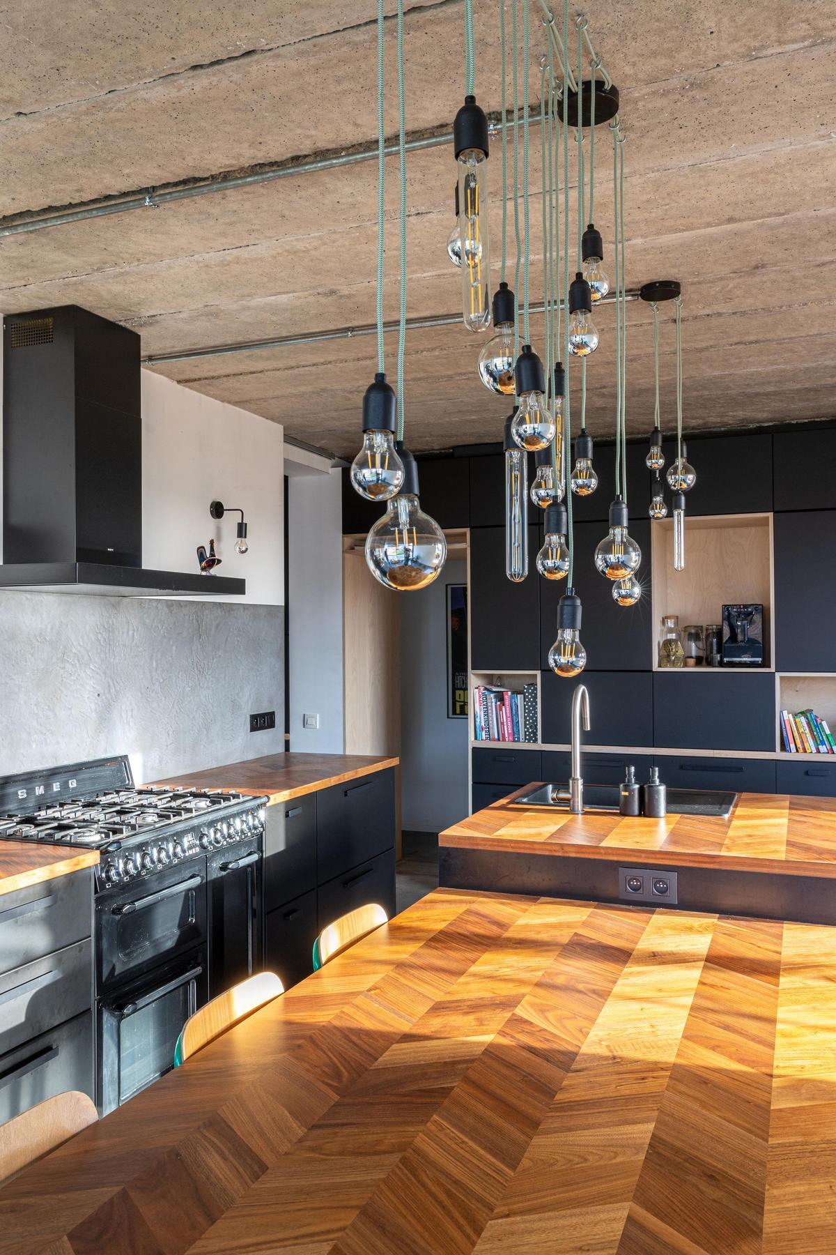 Cuisine moderne avec des armoires noires, des plans de travail en bois, une cuisinière à gaz et plusieurs suspensions ; motif géométrique en bois sur la surface de l'îlot.