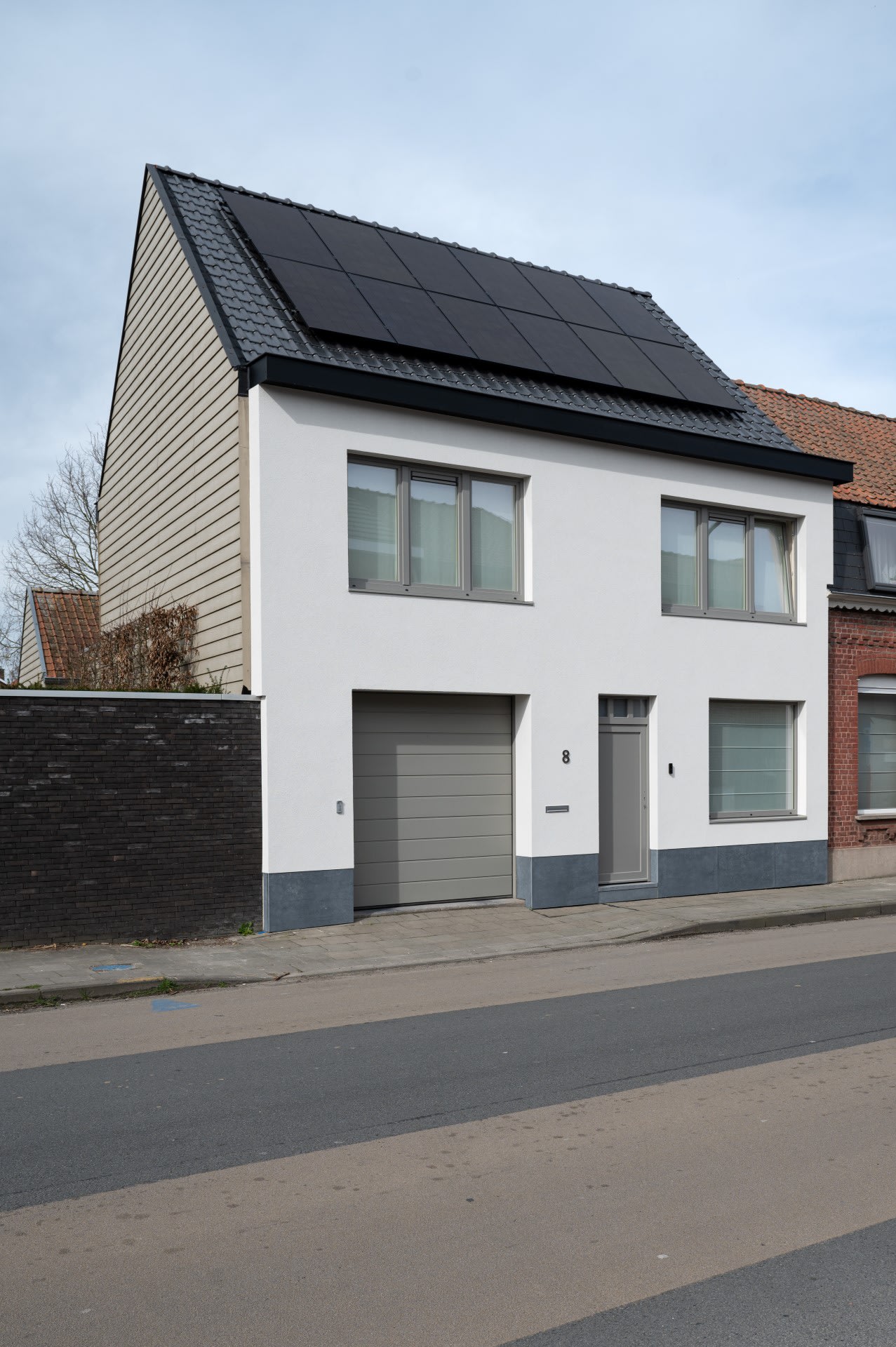 Une maison blanche avec un toit noir contrasté située dans un quartier calme