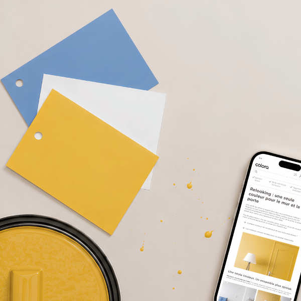 Sur une surface neutre se trouvent trois échantillons de peinture (bleu, blanc, jaune), un pot de peinture jaune, des éclaboussures de peinture jaune et un smartphone sur lequel s'affiche un site web consacré à la peinture.