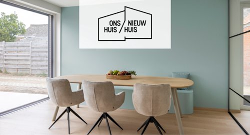 Een moderne eethoek met een houten tafel, drie beige stoelen, een fruitschaal en een muurkunstwerk met de tekst "ONS HUIS / NIEUW HUIS" in zwarte tekst.