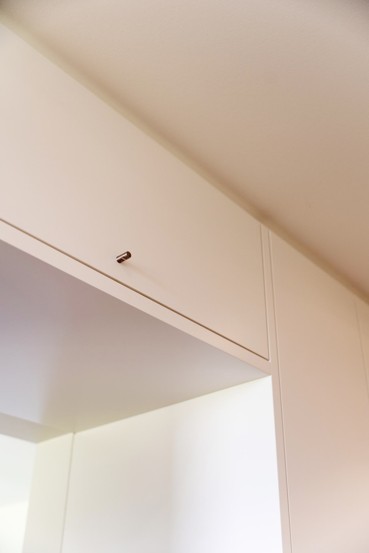 Gros plan sur une armoire blanche minimaliste, avec un petit bouton métallique sur la porte, fixée contre un mur et un plafond blancs.