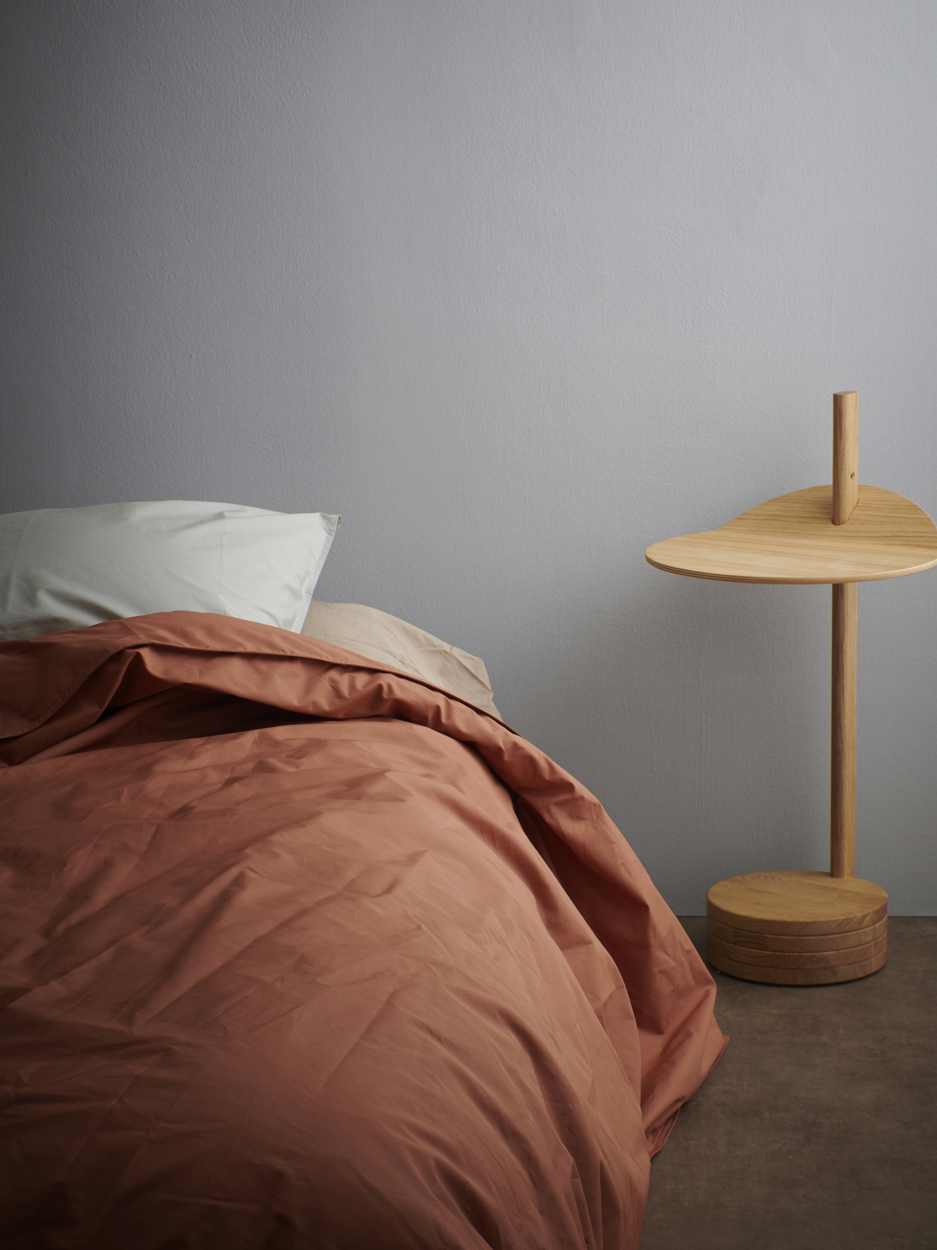 Colora- slaapkamer met warm grijze muren, houten nachttafel en laken in terracottakleur