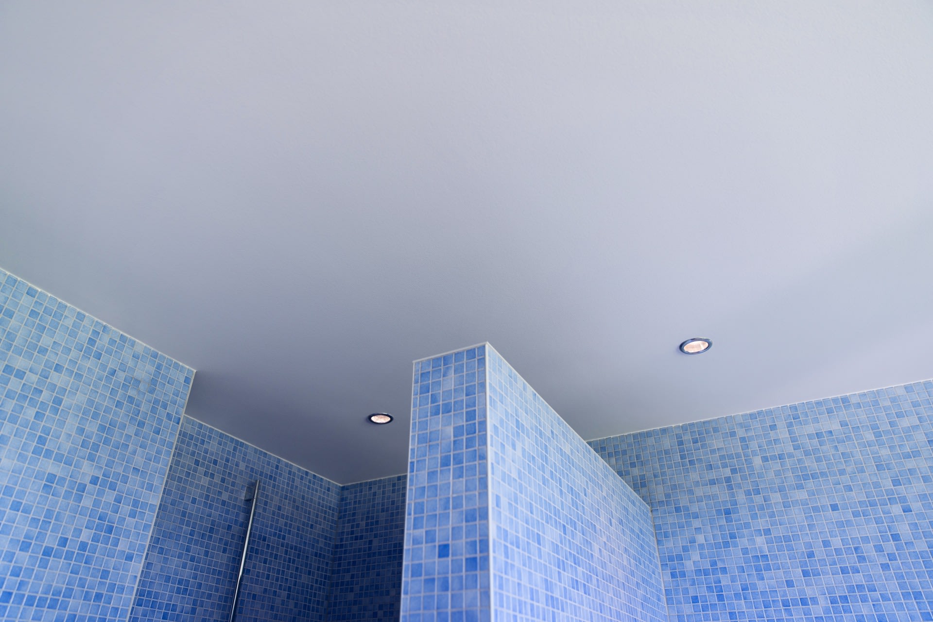 Salle de bains carrelée en bleu avec cloisons et éclairage encastré au plafond.