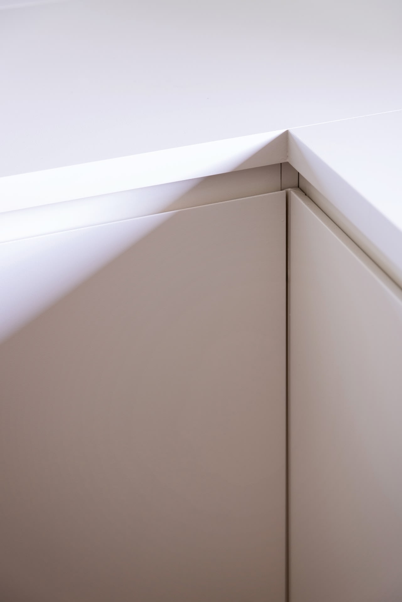 Gros plan sur l'angle de deux armoires blanches qui se rejoignent à angle droit, avec une lumière qui projette une ombre le long du bord.