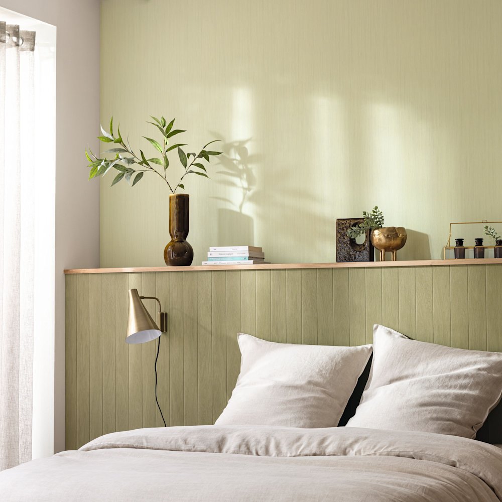 papier peint - chambre à coucher - Caselio - Woodline - WOD106857077 - vert - mur vert avec lambris, literie beige, étagère en bois avec décoration, vase avec branches, applique murale dorée