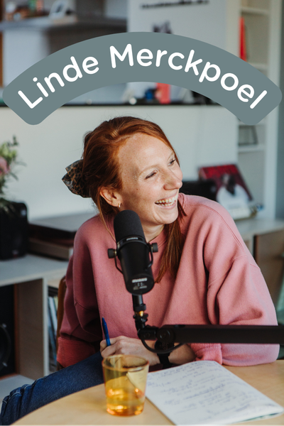 Een vrouw met rood haar, draagt een roze trui en lacht terwijl ze in een microfoon spreekt. Ze zit aan een tafel met notities en een drankje. Boven haar hoofd staat de tekst "Linde Merckpoel".