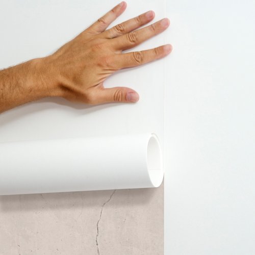 Une main caresse un rouleau de papier peint blanc sur un mur dont la texture est de couleur claire.