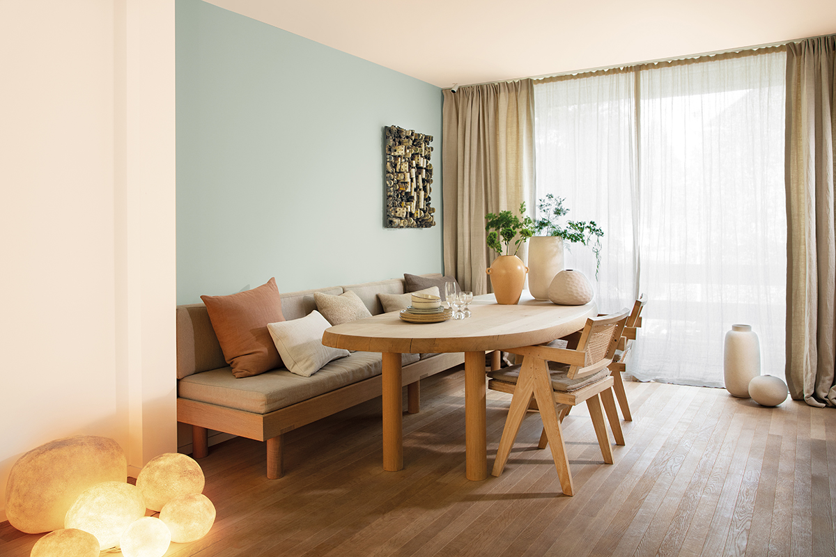 woonkamer met blauwe muur, houten tafel met zetel en houten stoelen, grijze gordijnen en houten vloer