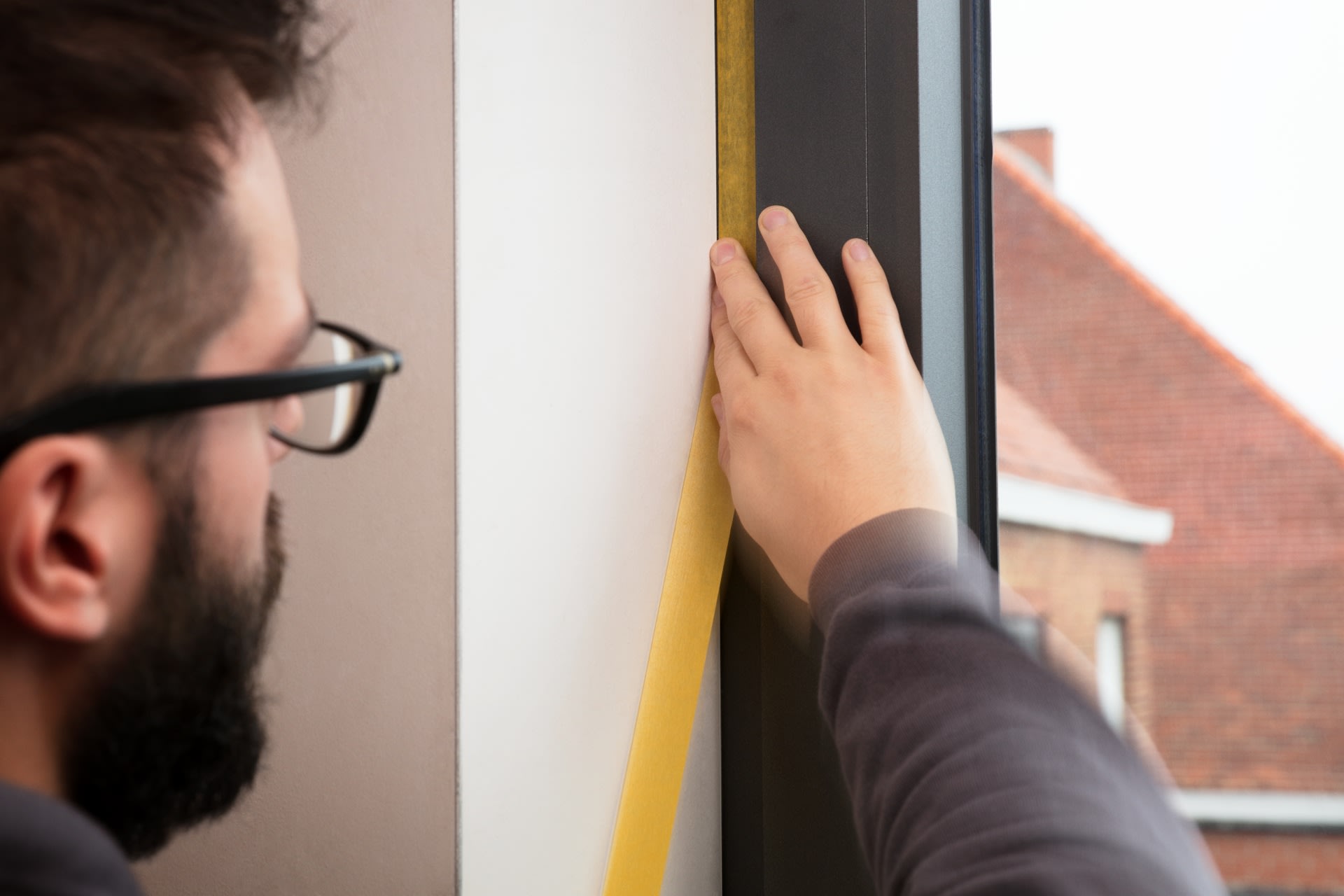 Quelqu'un applique du ruban de masquage le long du bord d'un cadre de fenêtre en prévision de travaux de peinture ou de rénovation.
