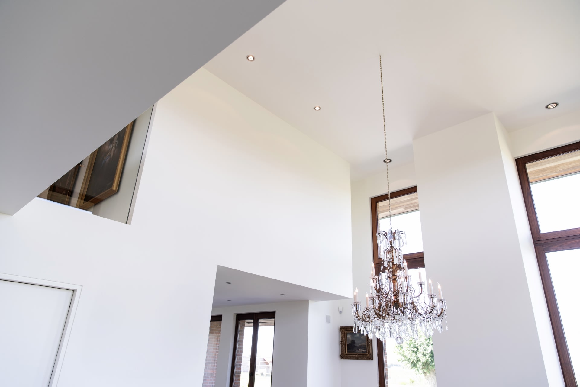 Intérieur spacieux et moderne avec de hauts murs blancs, de grandes fenêtres, un lustre en cristal et un tableau accroché au mur du fond.