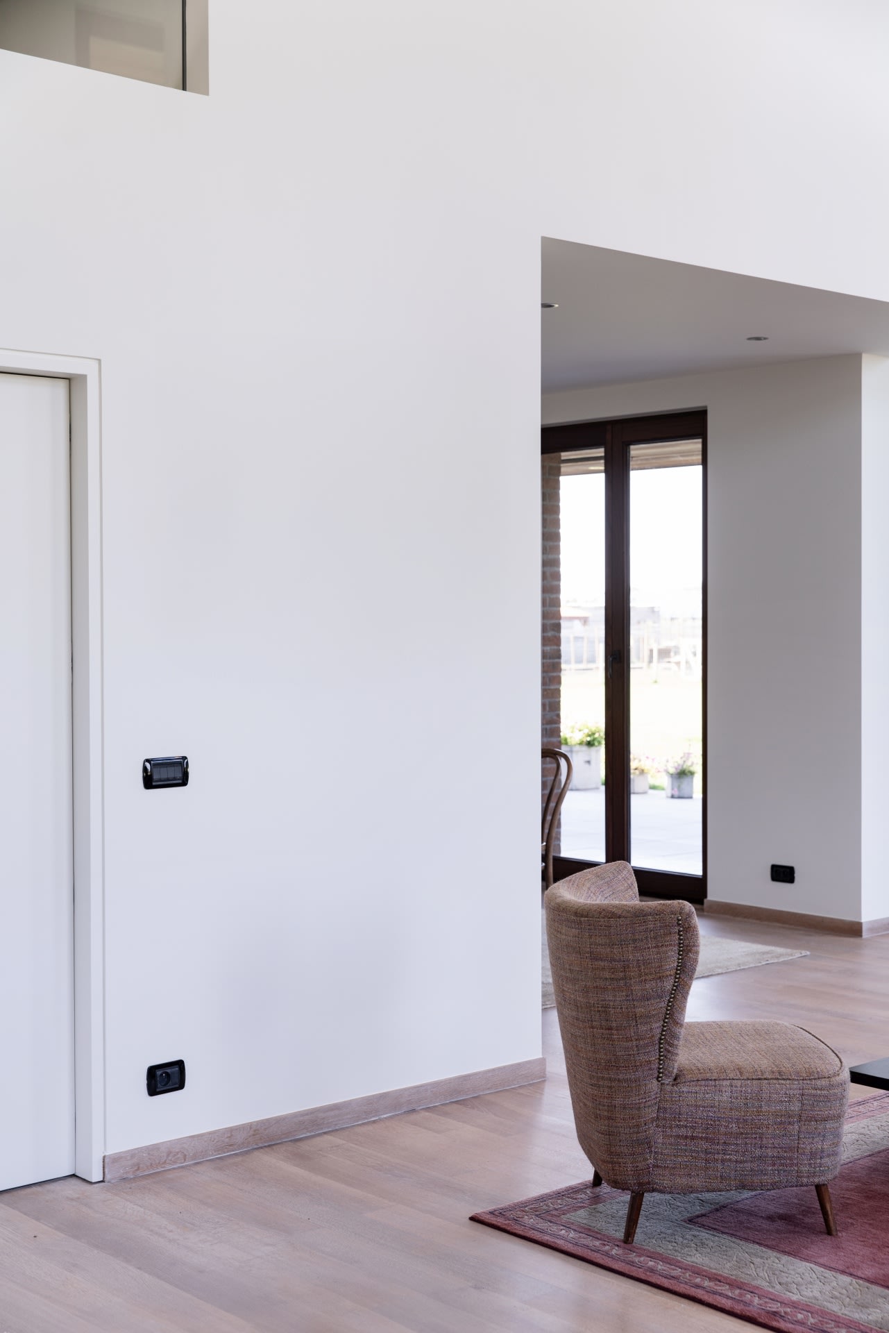 Un espace de vie moderne et minimaliste avec du parquet clair, des murs blancs, un fauteuil à carreaux et de grandes fenêtres donnant sur un espace extérieur.