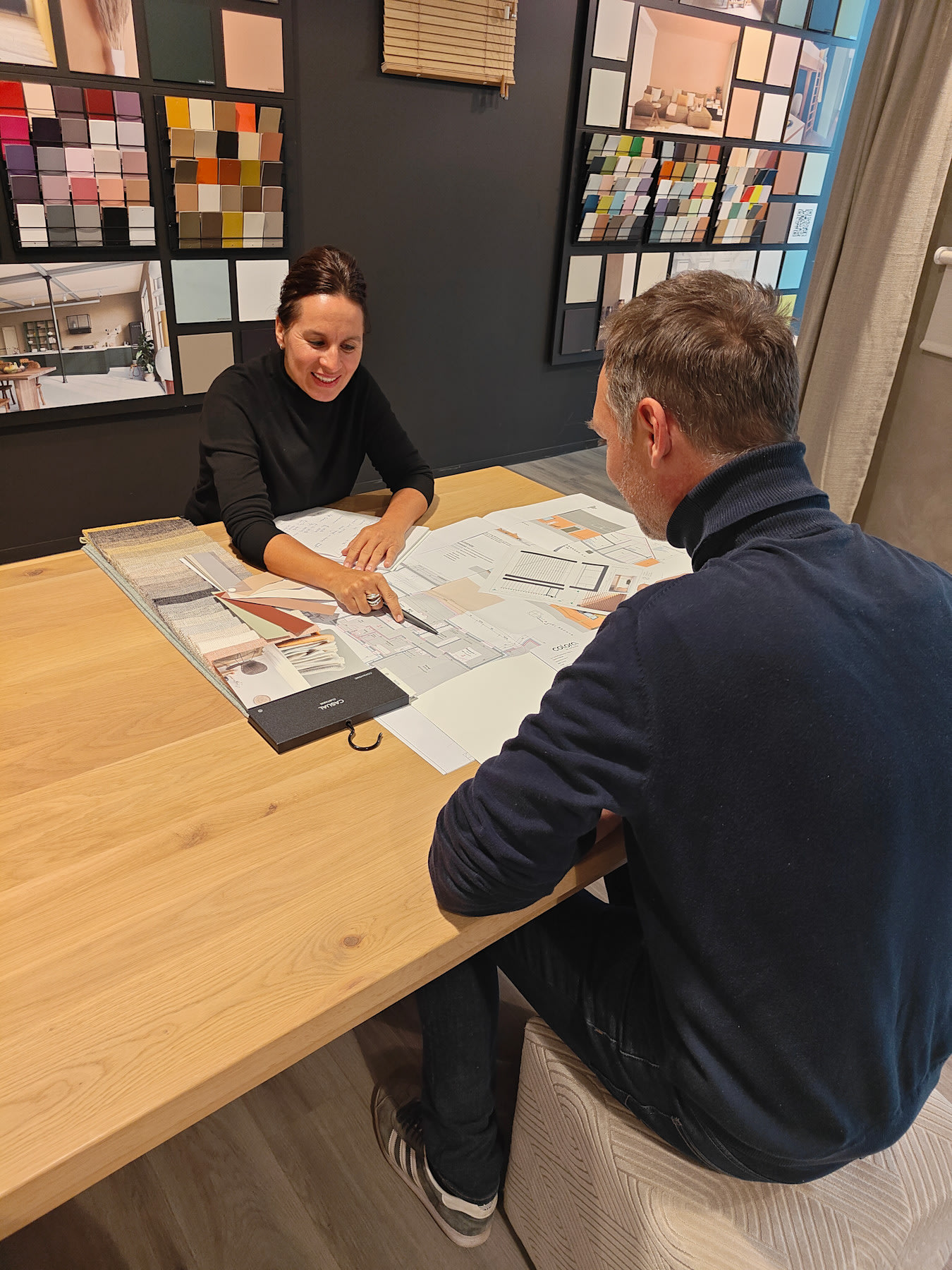 Beeld van kleuradviseur colora en klant aan tafel, ze bespreken de mogelijkheden in je interieur aan de hand van een kleurenkaart, behangstaal, kop koffie tijdens een Interieur Brainstorm Sessie in colora Deinze