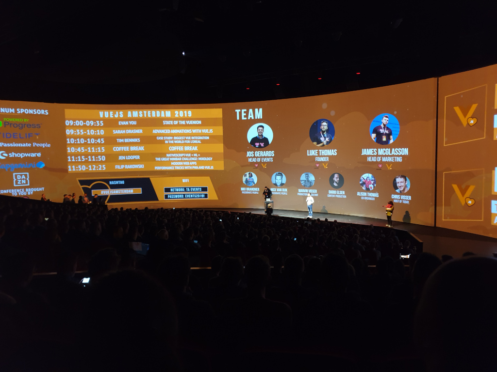 Photo of the big wide screen showing the timetable of the conference and team members of the Vue team