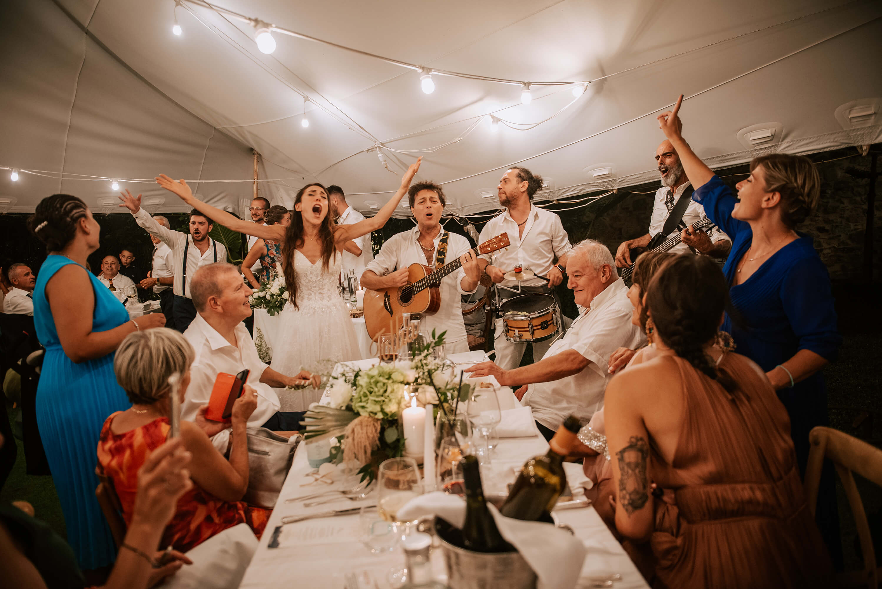 una foto della band Ambaradan che canta in mezzo ad i tavoli con la sposa durante il matrimonio alla locanda del cavaliere, a San Bartolomeo al Mare
