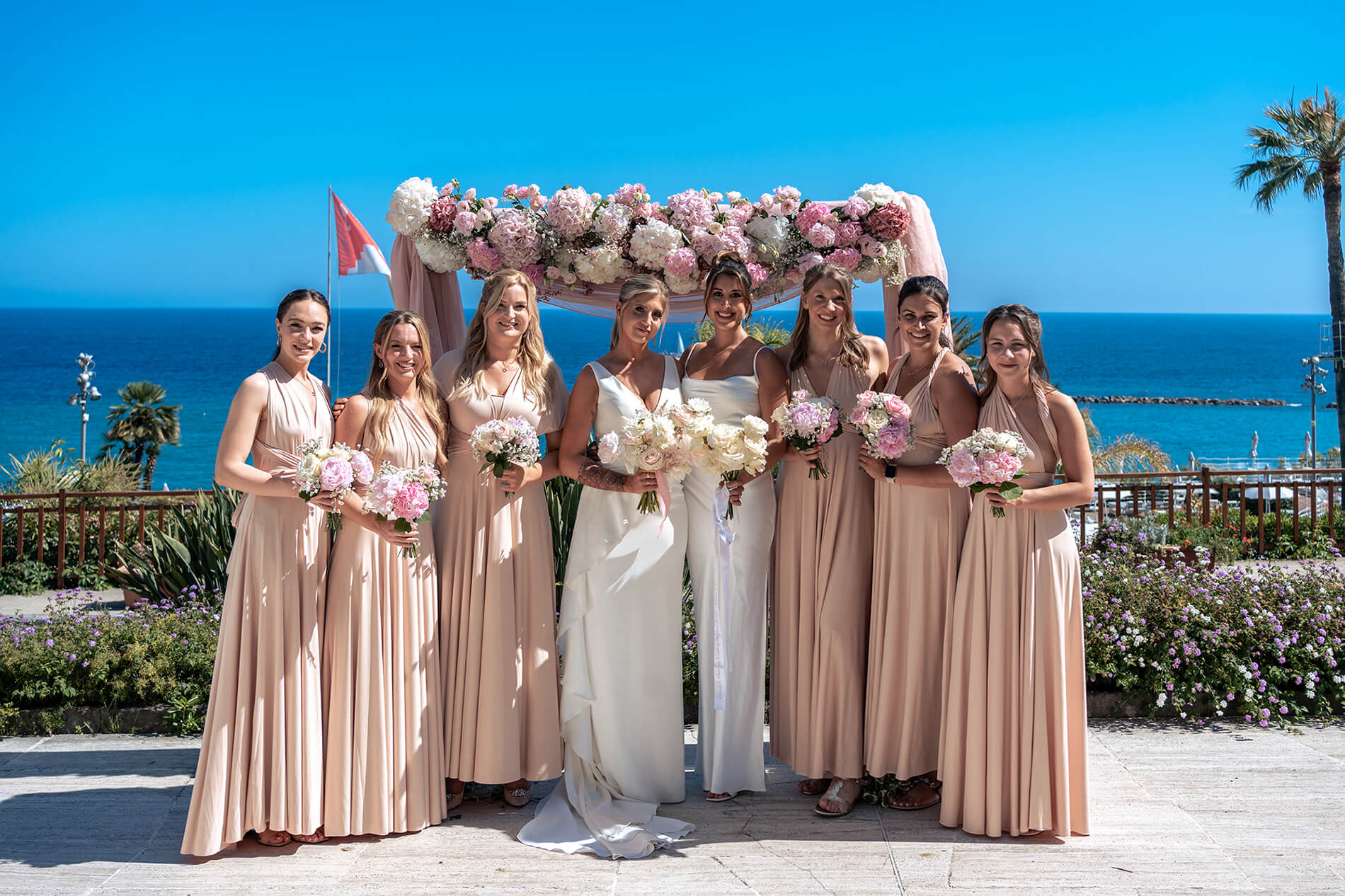 una foto delle spose e le damigelle davanti all'arco di fiori sulla terrazza dell'hotel royal di Sanremo.
