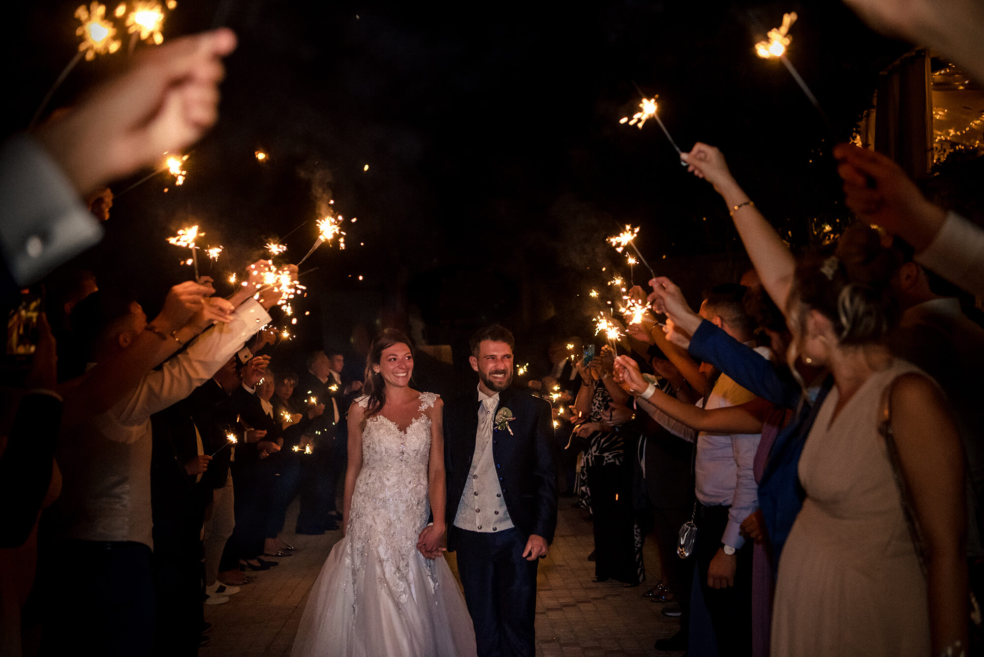 foto degli sposi passano in mezzo ad un corridoio di scintille tenute dagli amici, prima del taglio della torta, matrimonio in provincia di Imperia.