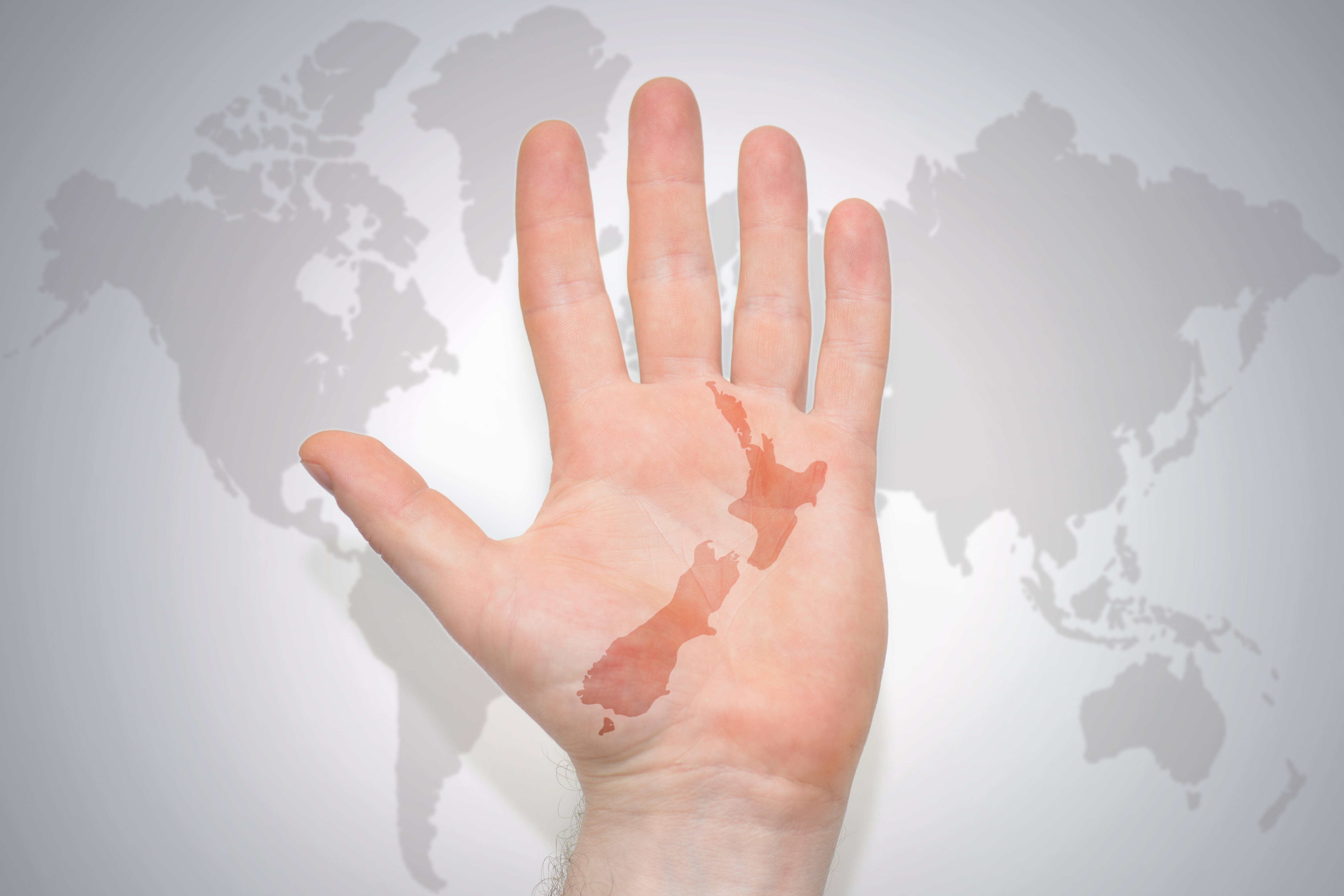Hand with an outline of New Zealand against a grey background of a world map