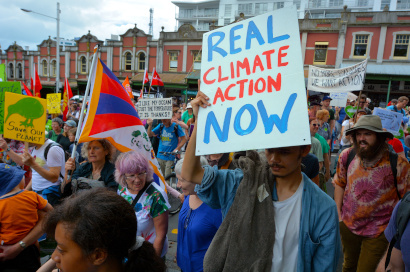 Scene of a street rally in Auckland 2015, with a 'Real Climate Action Now' poster as a focal point. 