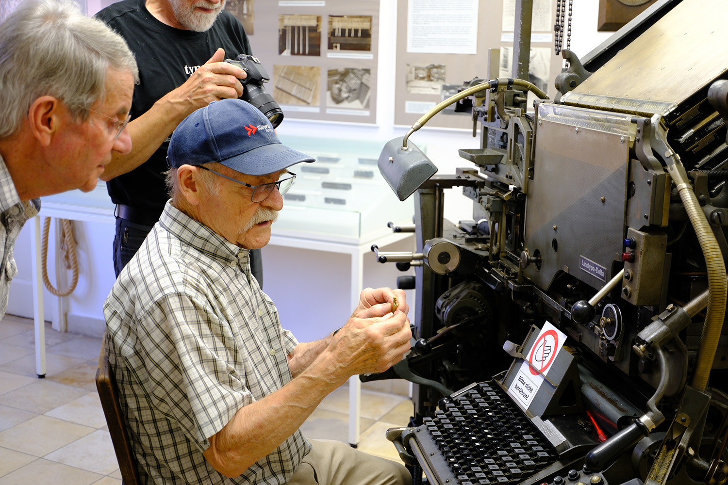 Horst demonstrating the Linotype and showing visitors a brass matrix