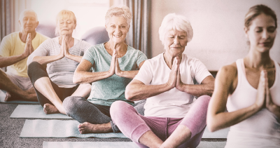 A group of elderly yoga practitioners lead by a female instructor.