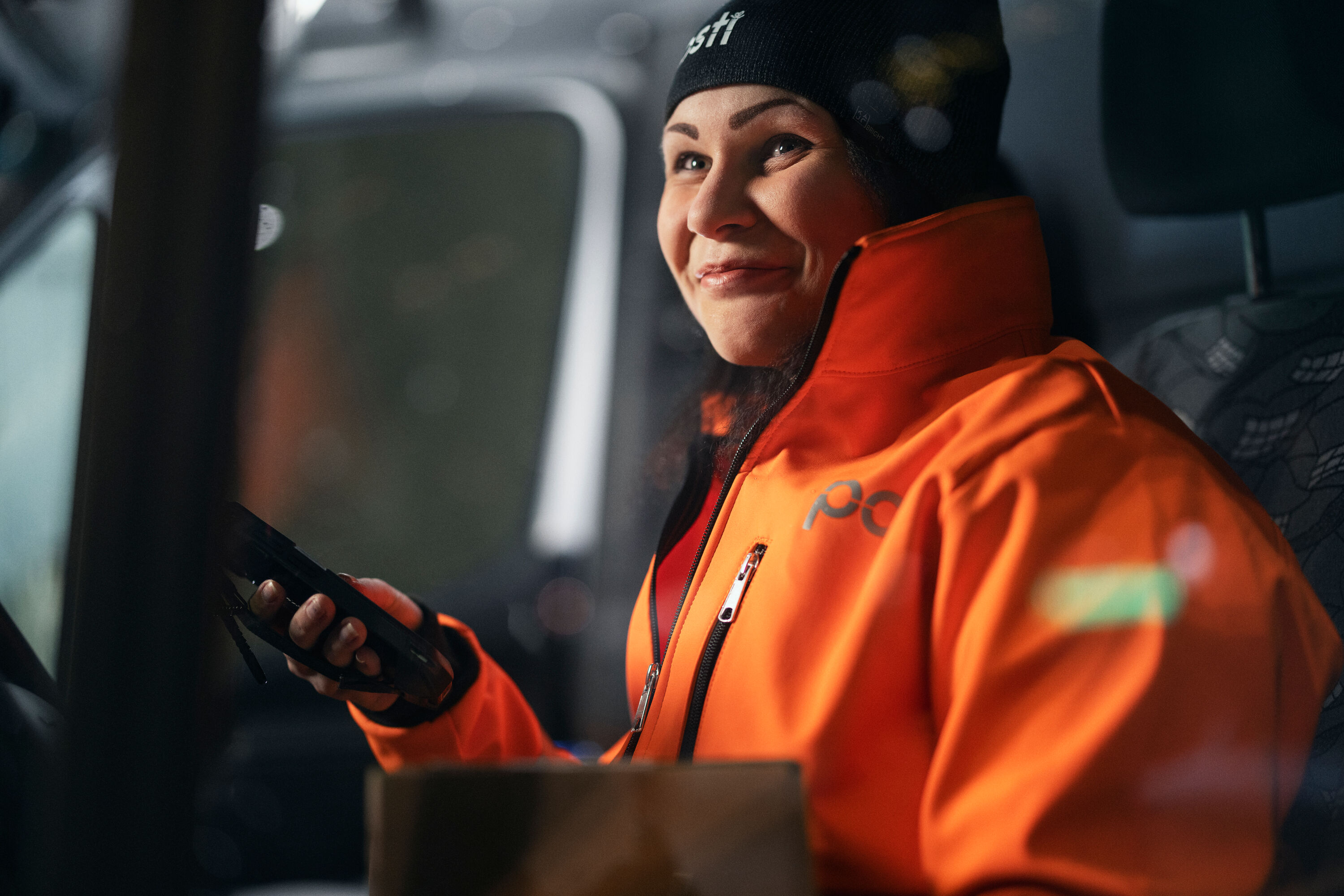 A Posti employee is sitting in a car and smiling.