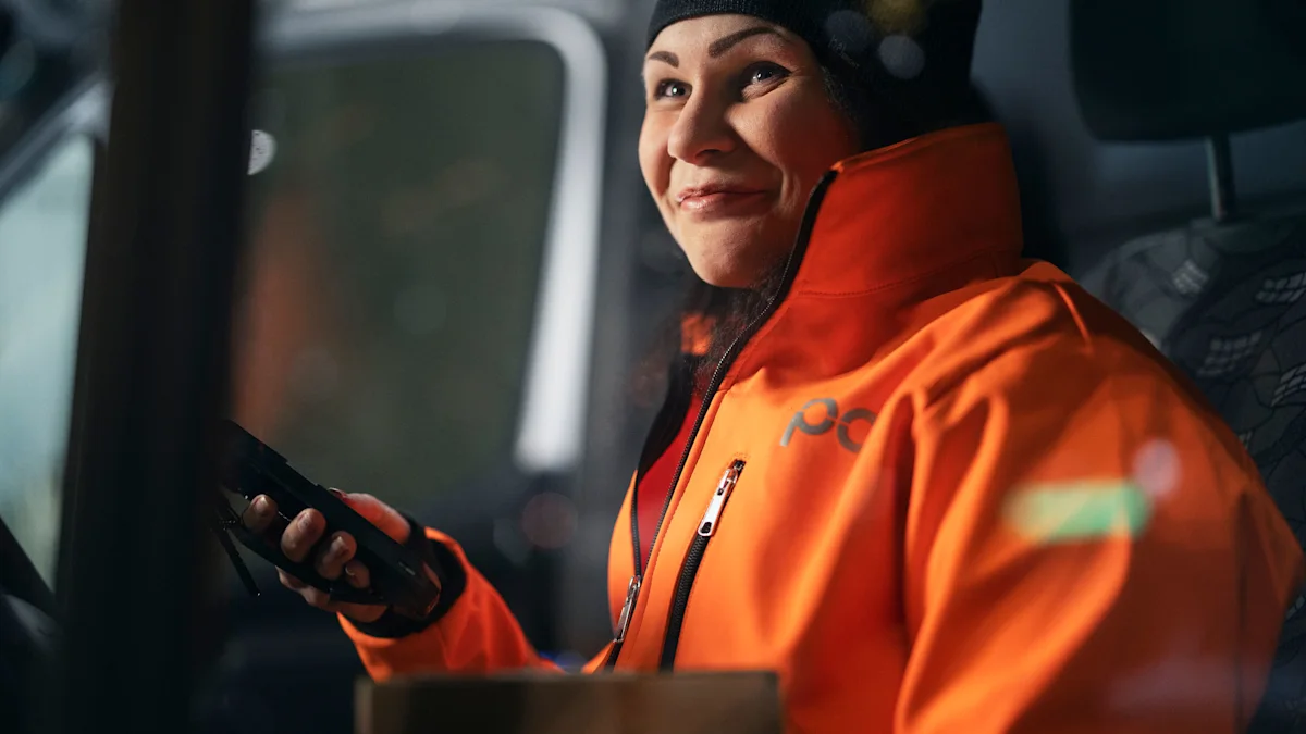 A Posti employee is sitting in a car and smiling.