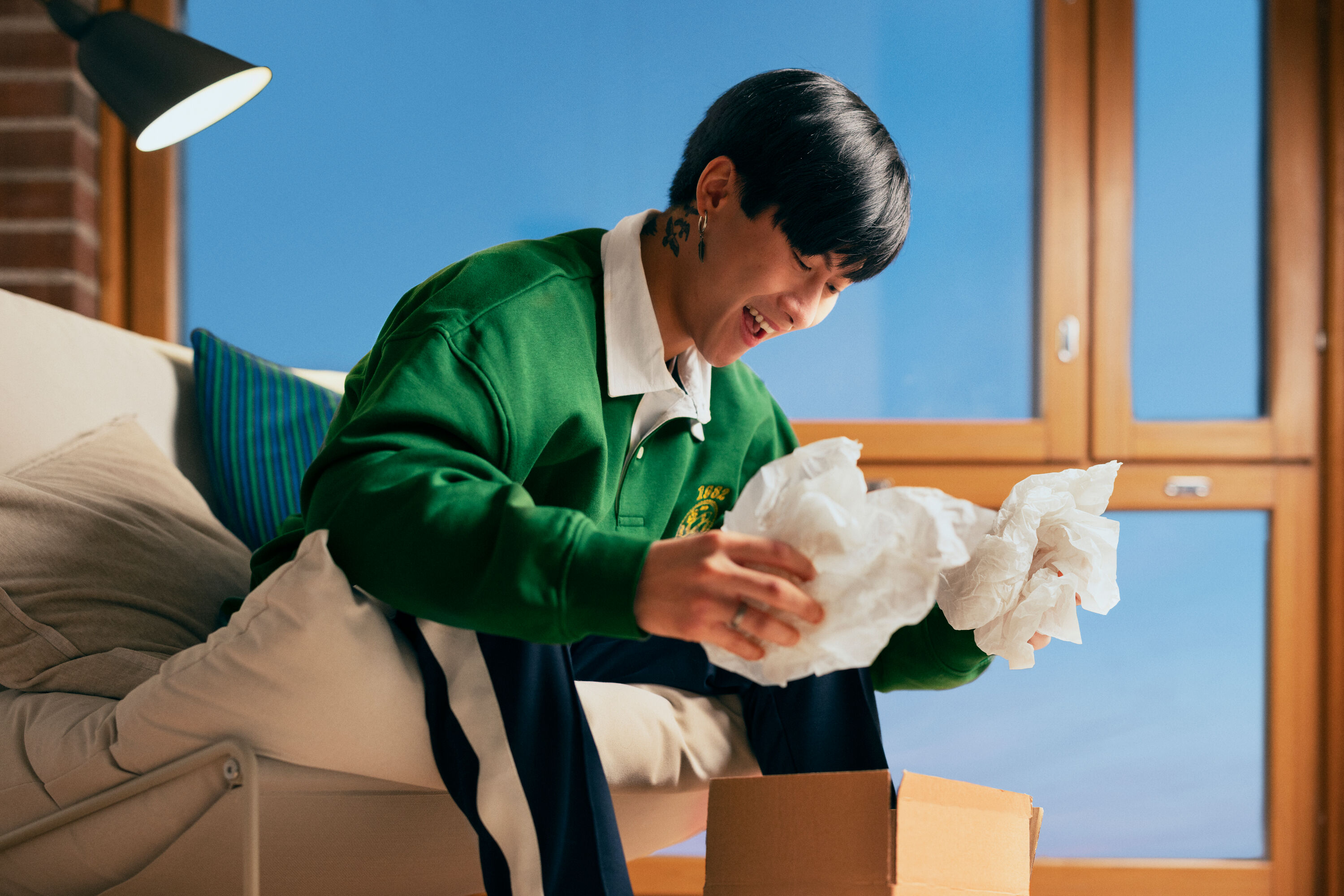 A smiling man is sitting on sofa and opening a package.