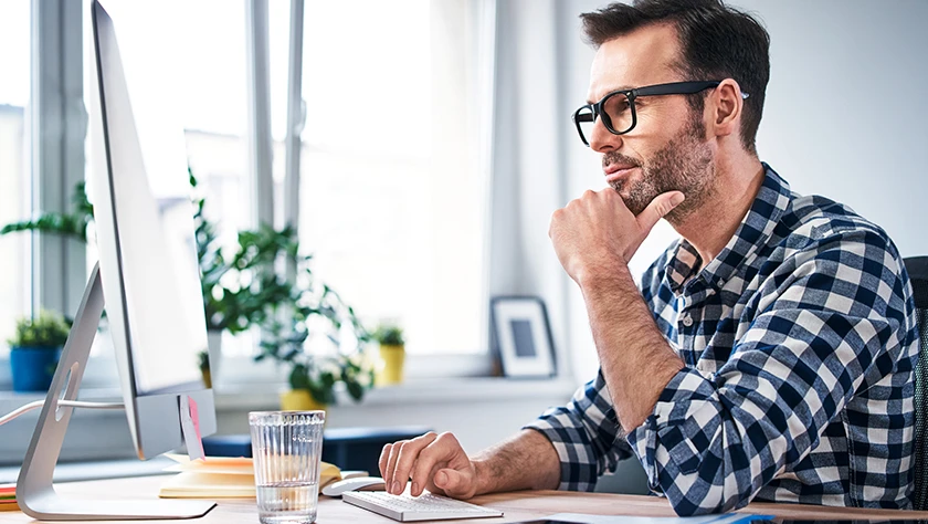 Man in glasses working on computer in a bright office.