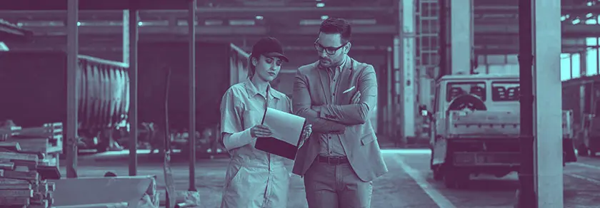 Two professionals discussing over a document in a factory setting.