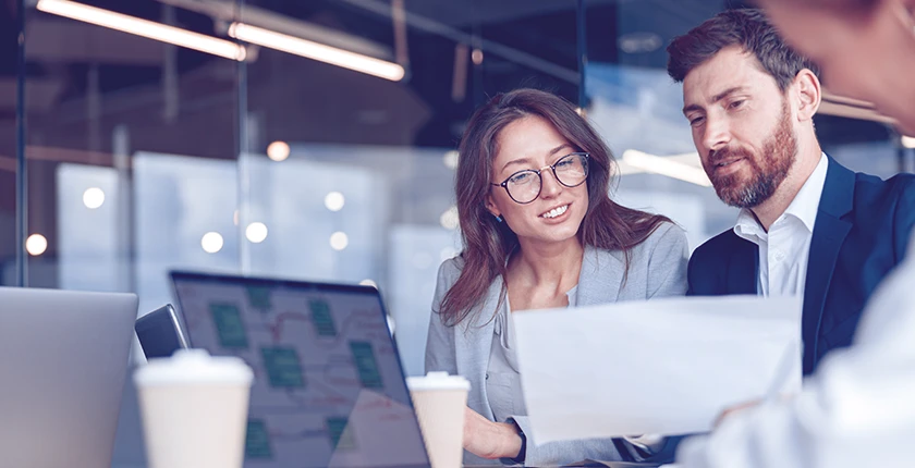 Two business professionals discussing work at a laptop in an office.