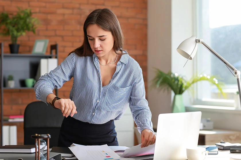 Woman in striped shirt checking time while working at desk.