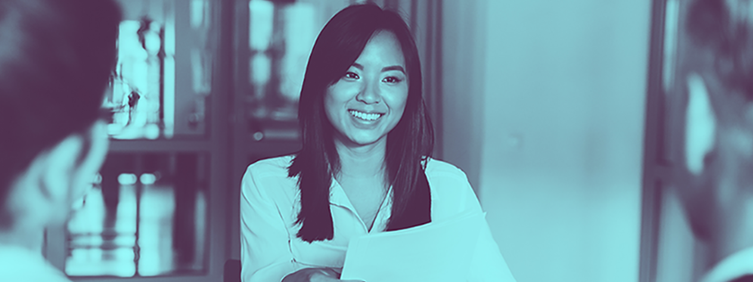 Asian woman smiling, holding papers in an office setting.