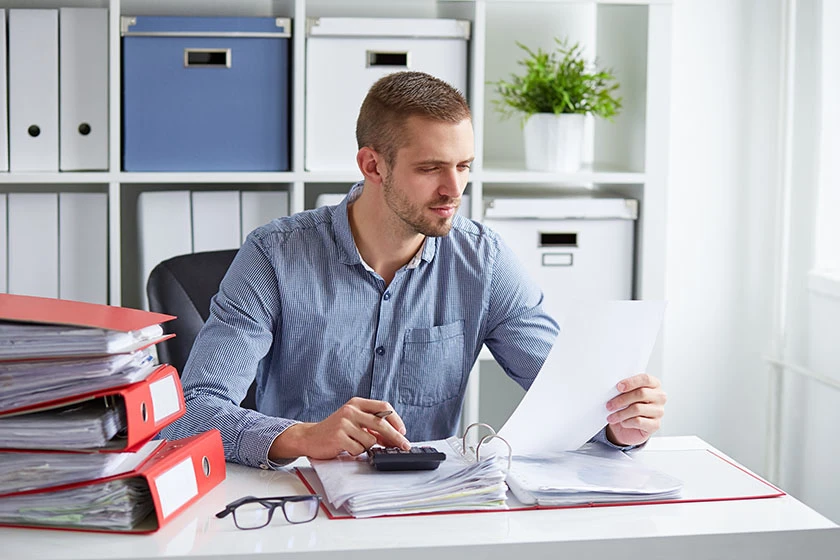 Man reviewing documents at office desk with calculator and binders.