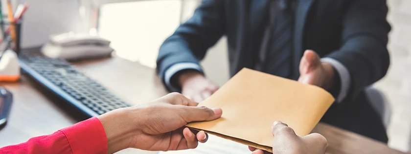 Two people exchanging a document across a desk.