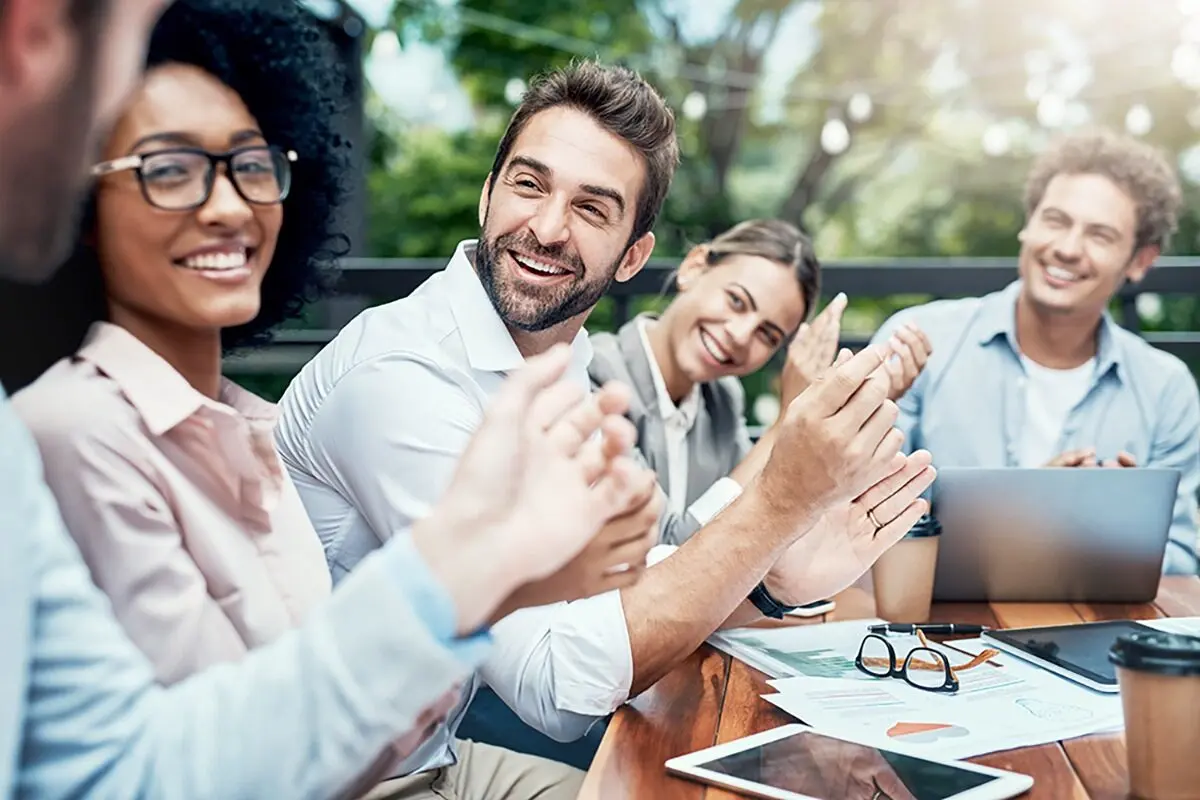 Group of diverse colleagues smiling and clapping at an outdoor meeting.