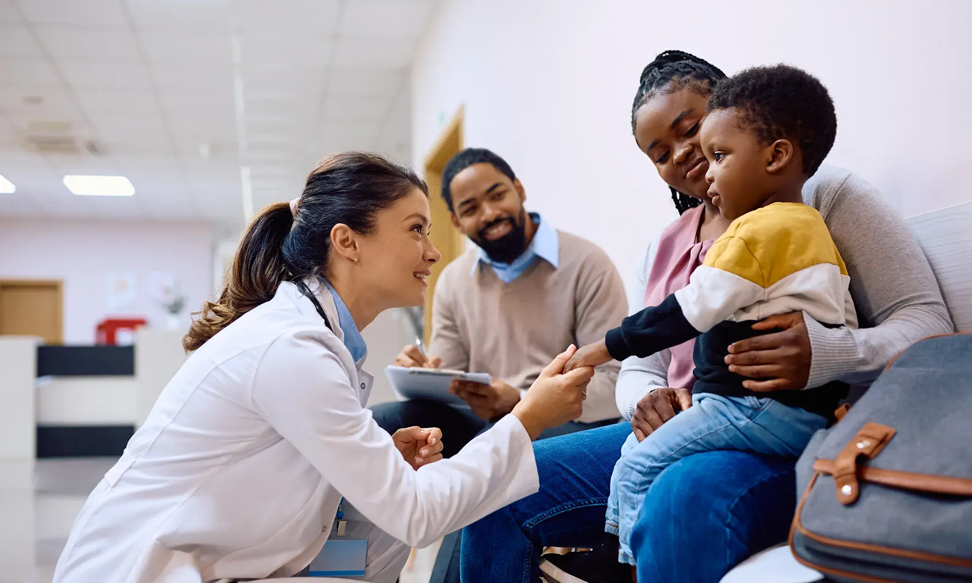 Caring healthcare provider crouches to connect with a child while the family looks on supportively.