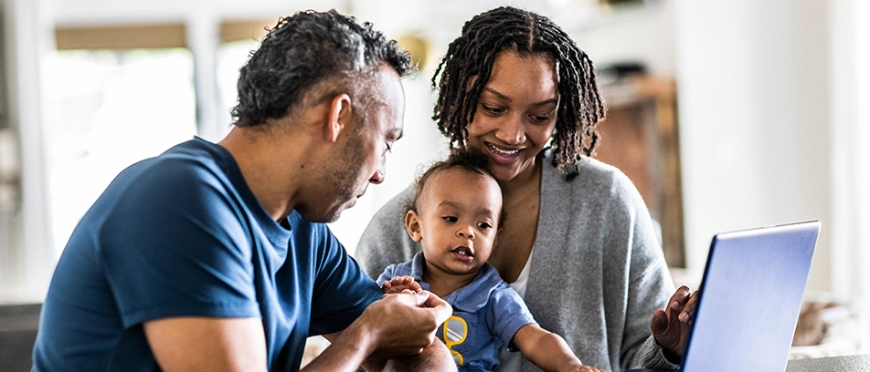 A young family reviews trusted health information together on their laptop while caring for their baby.