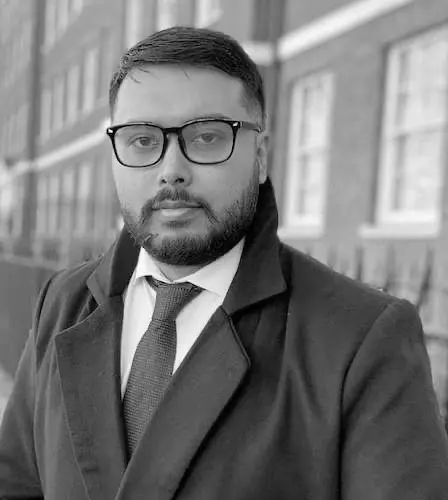 Black and white photo of Solicitor Shaheen Mamun in a suit and tie standing in front of a building.