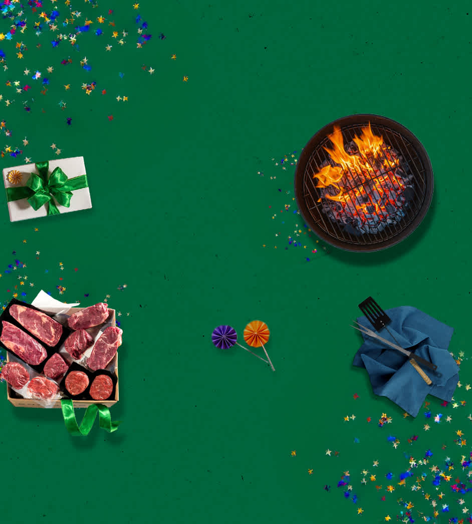 Meat gift box full of beef cuts next to a charcoal grill on a green background