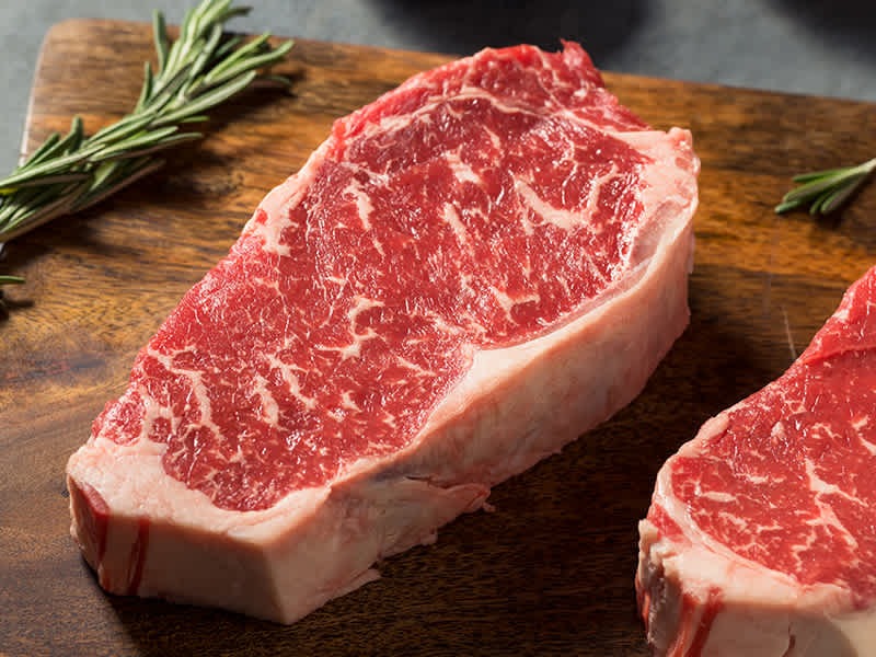 Uncooked steak sitting on wooden cutting board.