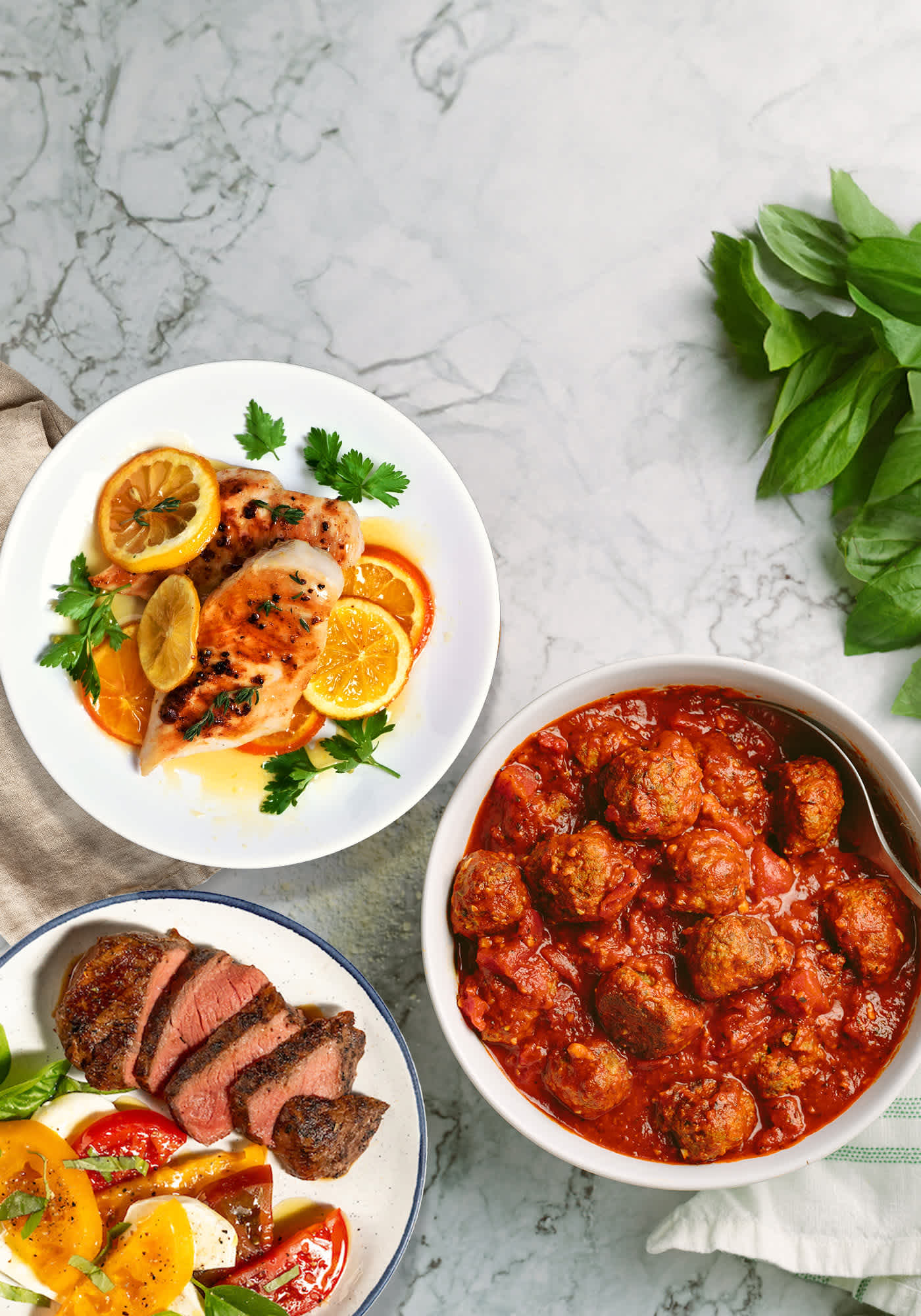 Plated chicken, meatballs, and steak on marble background