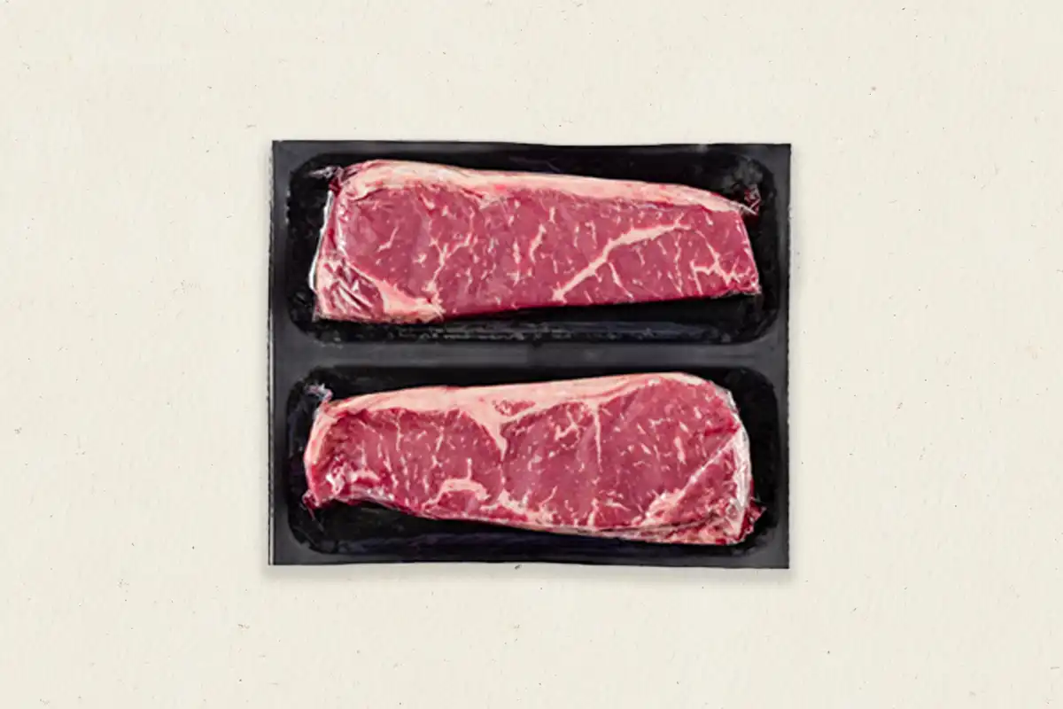 Two raw New York strip steaks in plastic packaging
