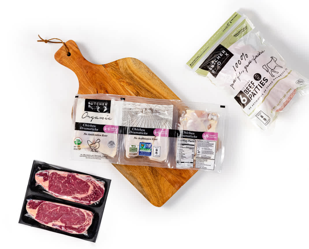 Ribeyes, drumsticks and burgers in packaging on a wooden cutting board