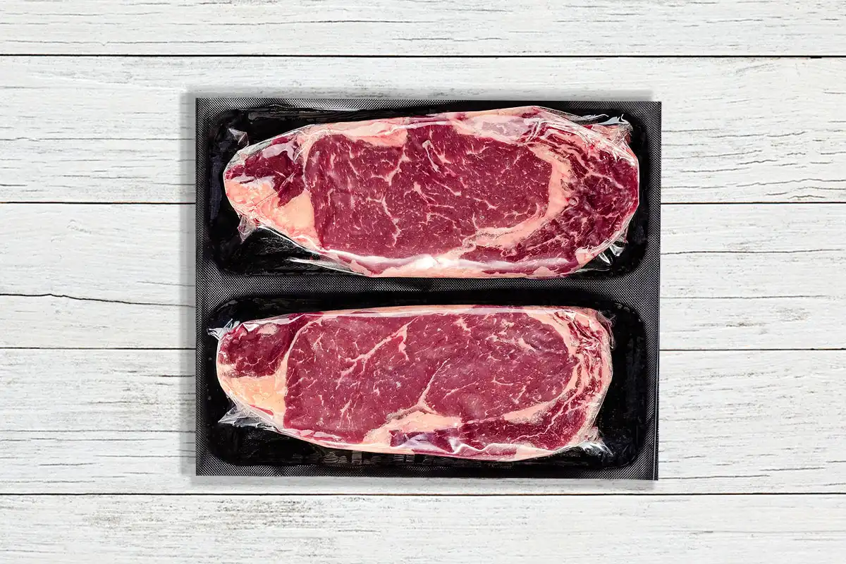 Packaged ribeyes on wood background
