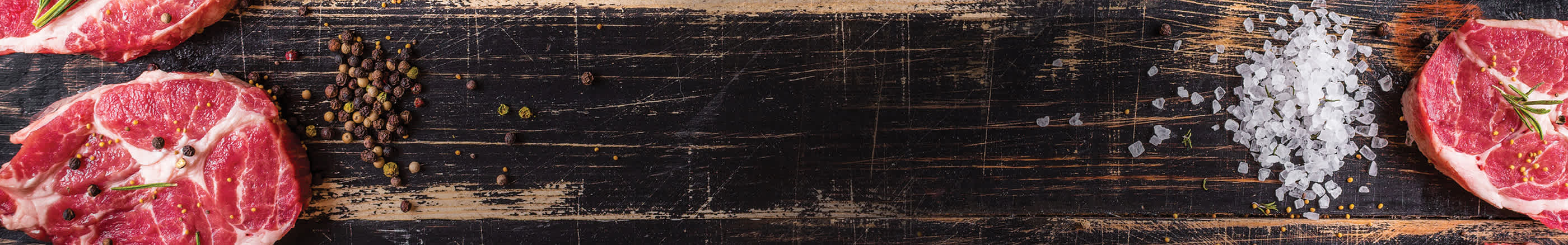 Steaks on a wood cutting board surrounded by salt and peppercorns