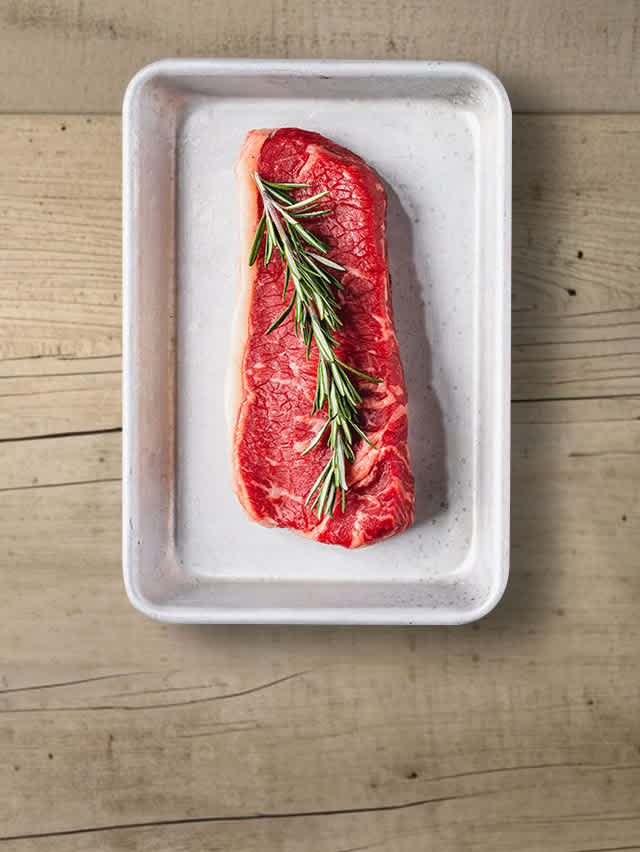 A raw steak on an aluminum tray, topped with aromatic rosemary.