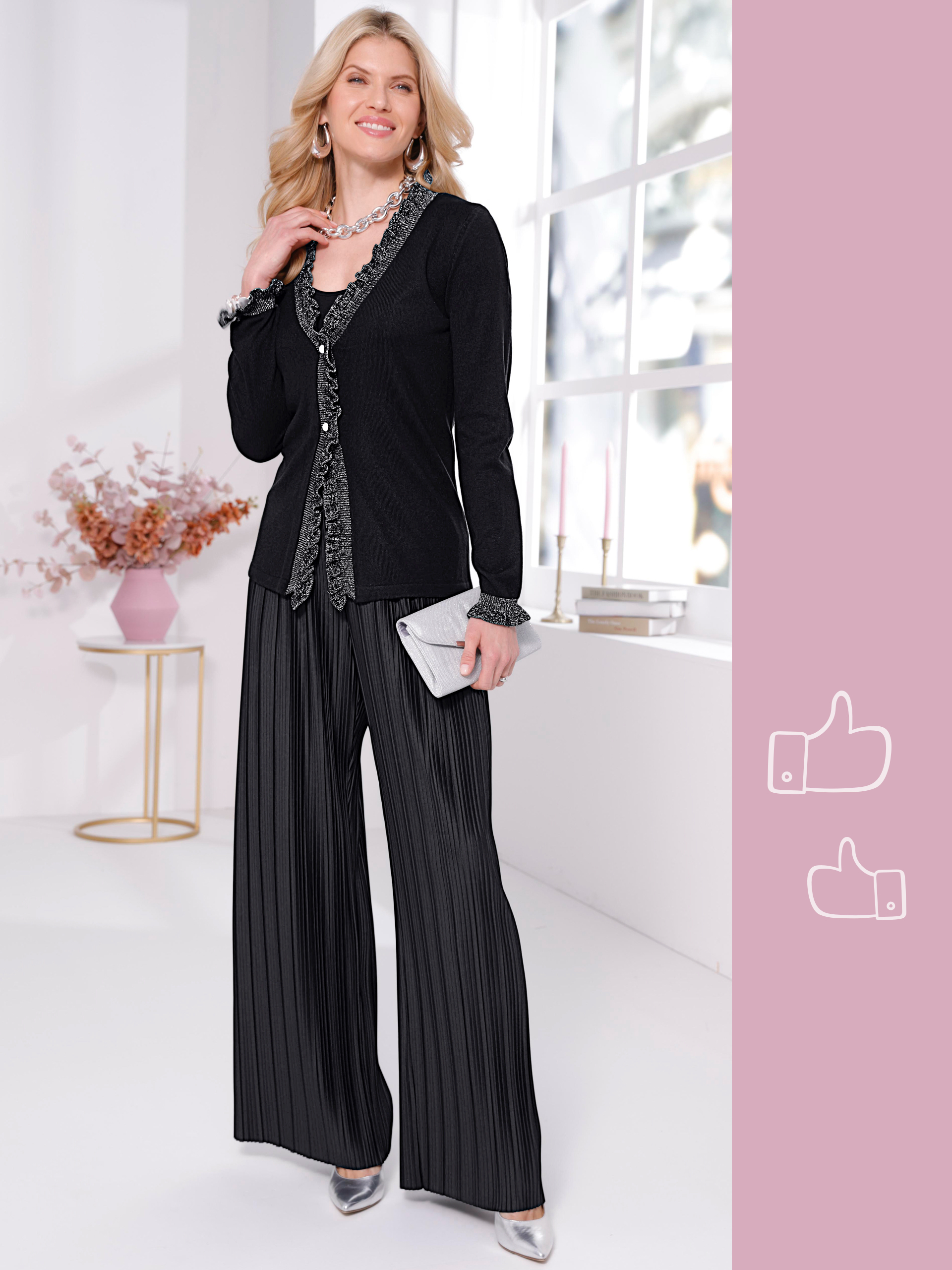 Ein Model trägt einen schwarzen Blazer, eine silberne Bluse und schwarze, weite Hosen, hält eine silberne Clutch.