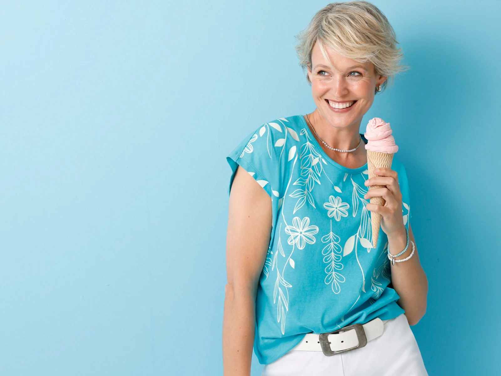 Ein Model trägt ein türkisfarbenes Shirt mit weissem Blumenmuster und hält ein rosa Eis in der Waffel.