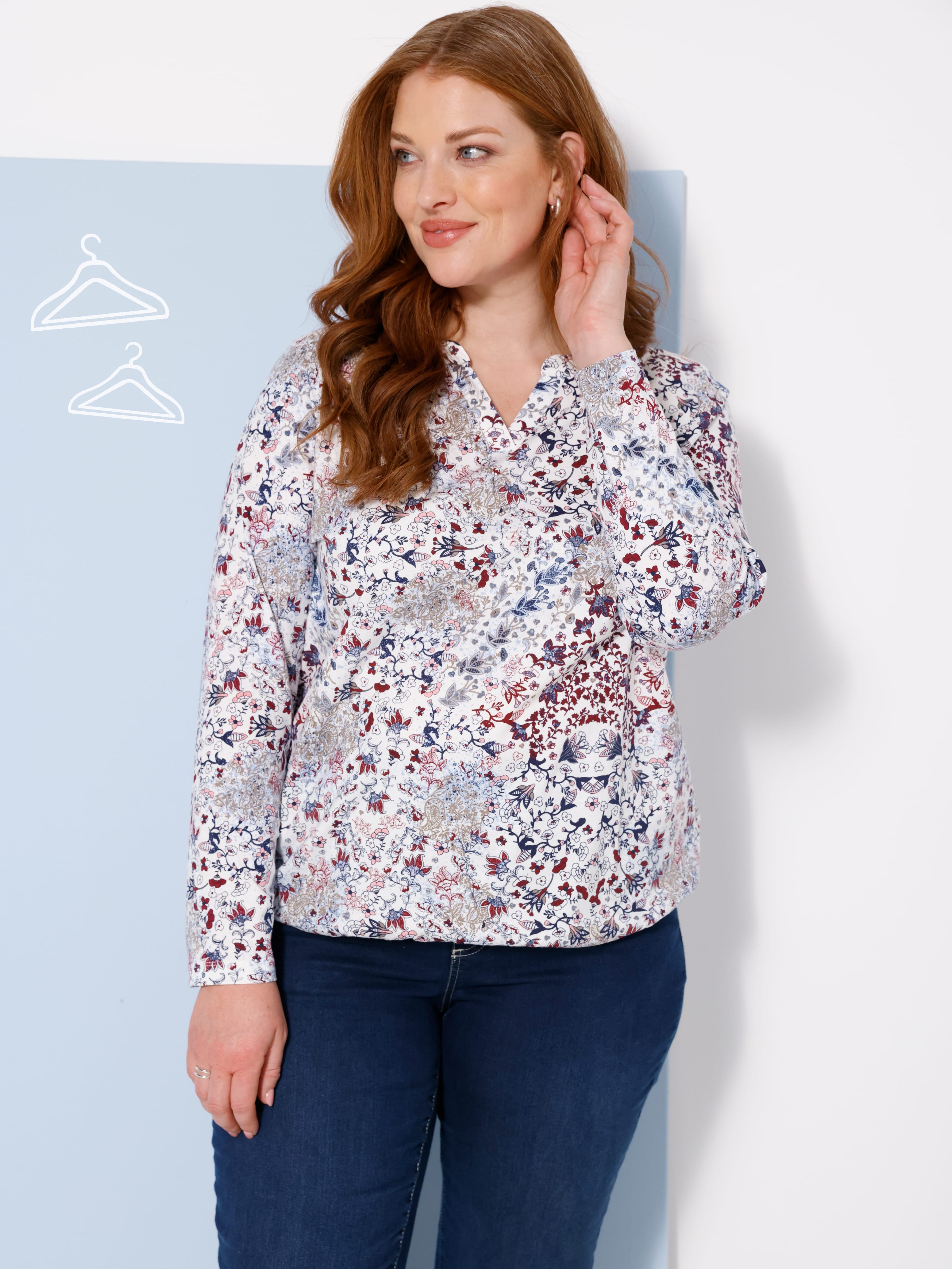 Ein Model trägt eine weiß gemusterte Bluse und dunkelblaue Hose.